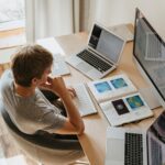 Top view of young programmer working on multiple laptops in a modern office setting.